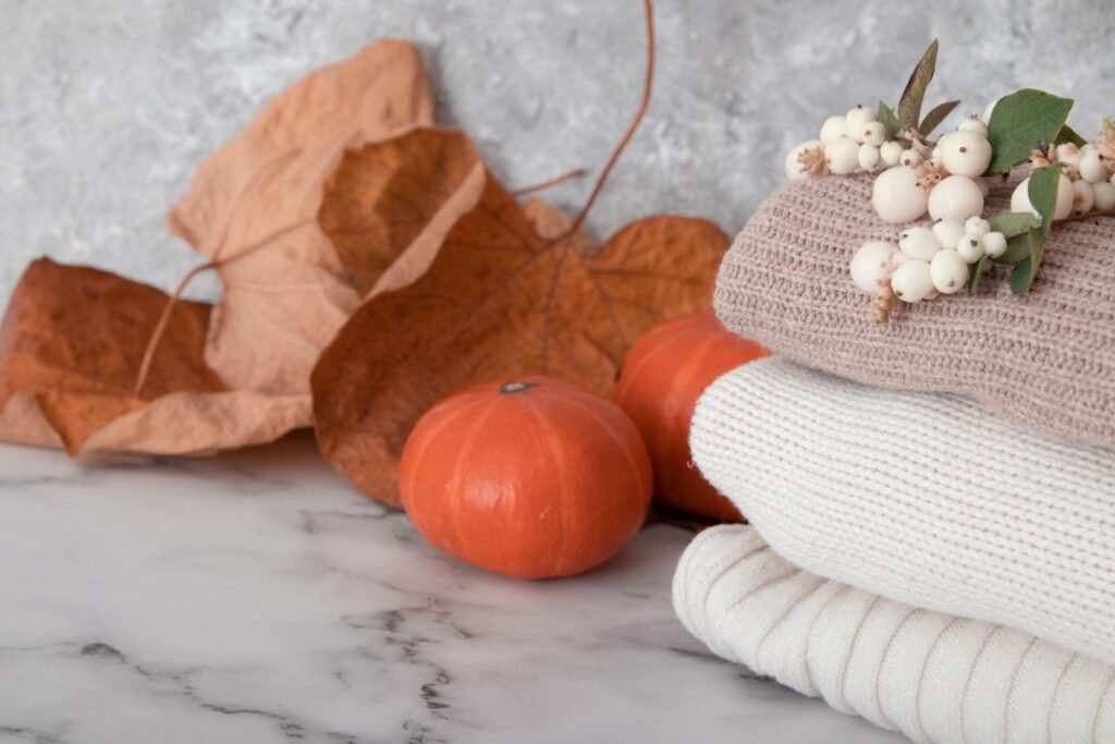 Two small pumpkins, some leaves, some comfy sweaters and snowberries sit on top of a marble countertop